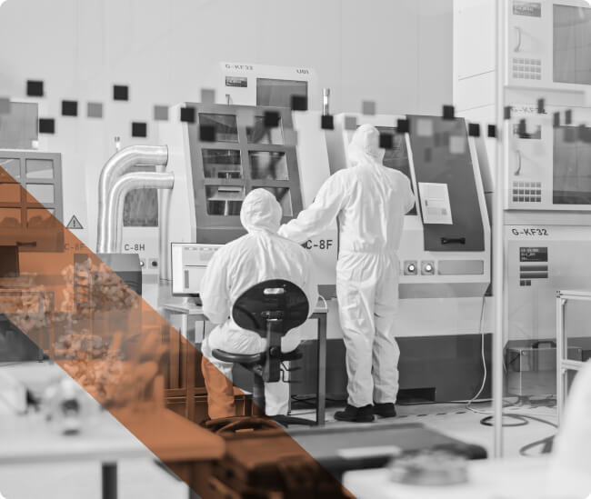 Two laboratory professionals wearing protective medical coveralls work at a large piece of laboratory equipment.