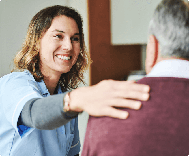 A smiling medical professional in scrubs puts her hand on her patient's shoulder.